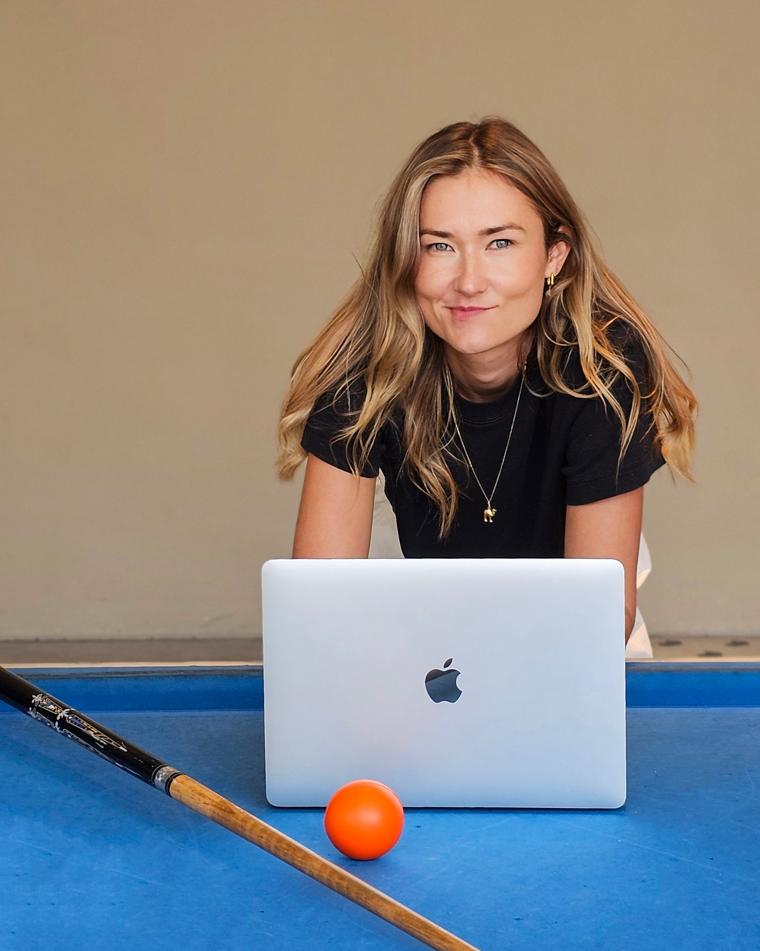 Sintija Capel, founder of June19, leaning on a pool table behind a laptop with an orange ball
